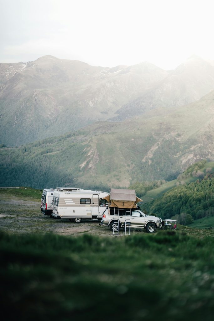 A car and camper van set up camp in a serene mountainous landscape, perfect for an adventurous escape.