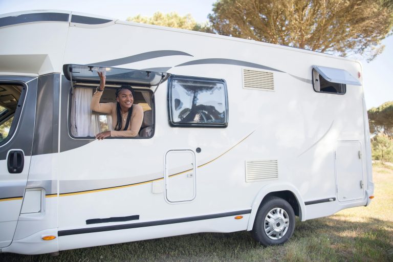 A woman smiles from a motorhome window during a sunny road trip in Portugal.