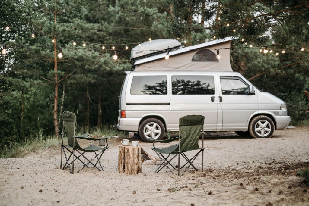 Tranquil forest campsite featuring a van, chairs, and string lights.